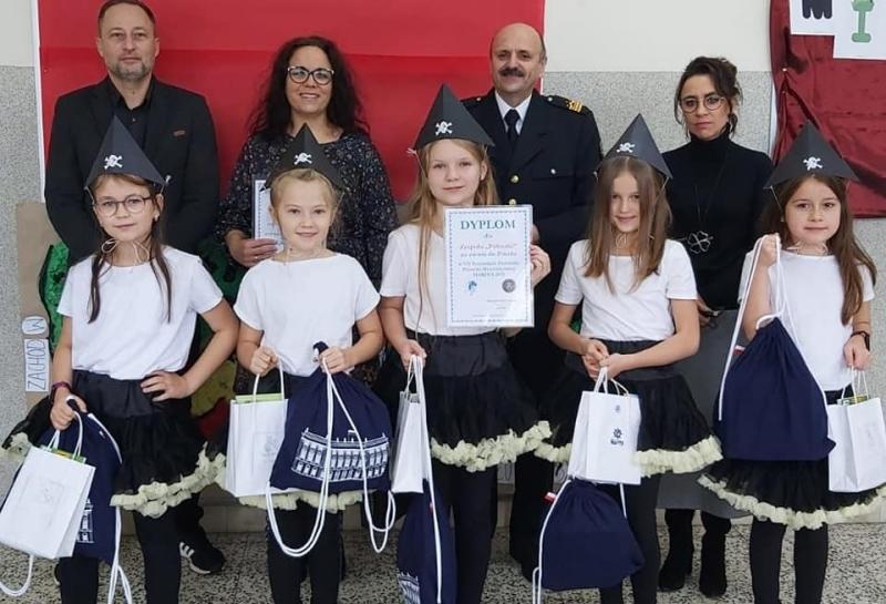 Na pierwszym planie uczennice zespołu "Półnutki" z dyplomami, ubrane w stroje marynarskie. Na drugim planie dyrektor szkoły, nauczycielka przygotowująca do konkursu i organizatorzy konkursu.