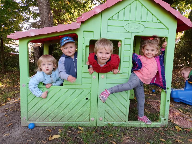 Uśmiechnięte dzieci wyglądające z okien plastikowego domku znajdującego się na placu zabaw