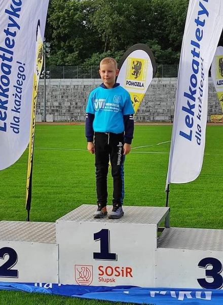 Uczeń stoi na pierwszym miejscu podium, w tle zielona murawa boiska