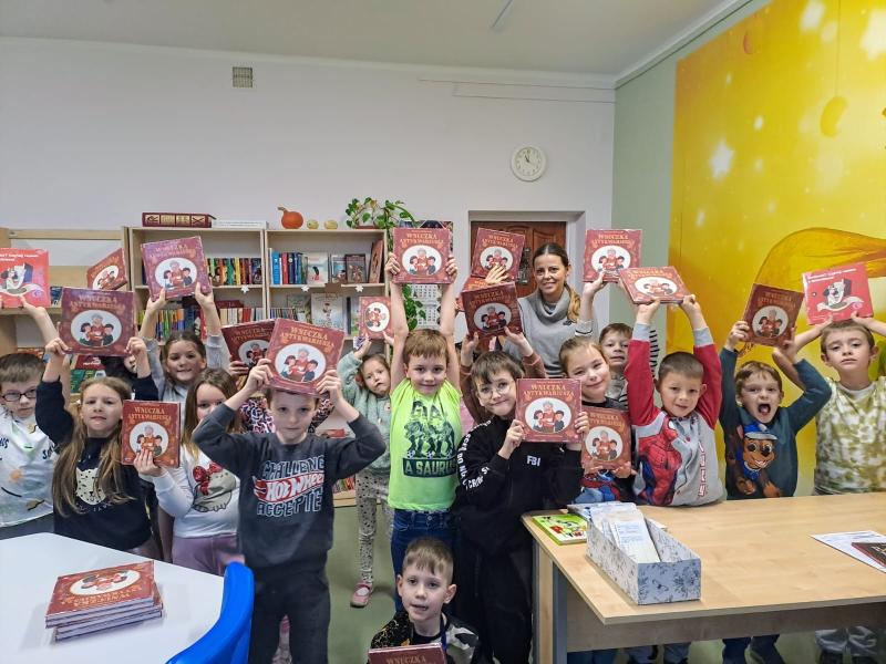 Biblioteka szkolna - uczniowie unoszą do góry otrzymane książki.