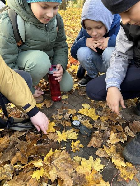 Uczniowie operują kompasem umieszczonym na ziemi podczas wyjścia do parku