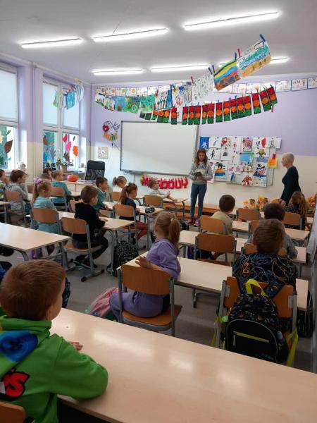 Uczennica klasy szóstej czyta książkę uczniom edukacji wczesnoszkolnej.