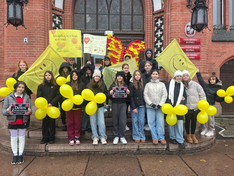 Dzień Życzliwości - zdjęcie przed Urzędem Miasta. Uczniowie z żółtymi balonikami i banerami.