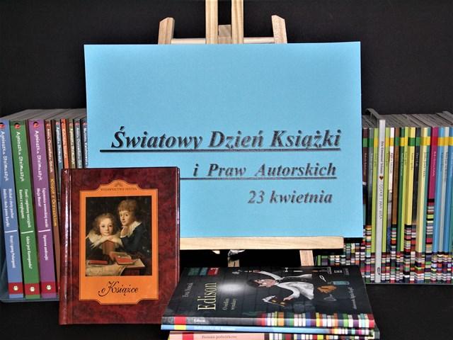 Na tle kolorowych książek ustawiony jest stelaż z plakatem koloru niebieskiego z napisem Światowy Dzień Książki i Praw Autorkich 23 kwietnia