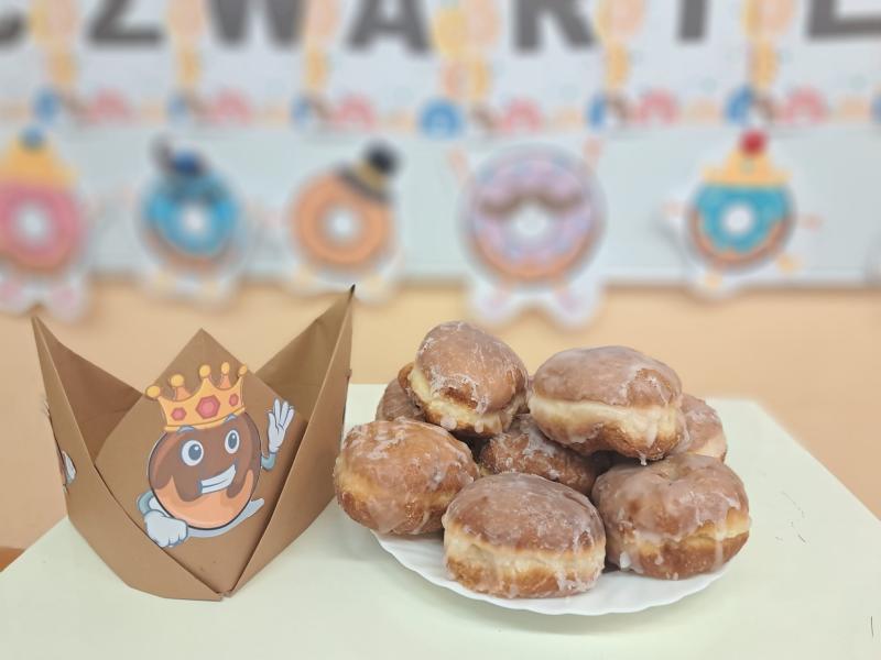 Po prawej stronie pączki ułożone na talerzu, po lewej papierowa korona Kr&oacute;la Pączk&oacute;w.