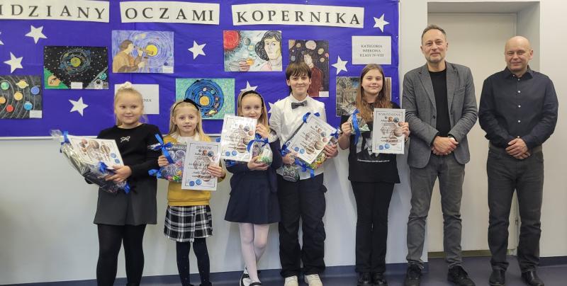 Nagrodzeni i wyr&oacute;żnieni uczniowie z dyrekcją szkoły. W tle nagrodzone prace uczni&oacute;w.