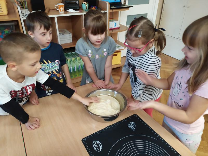 Dzieci stoją wokół dużego stołu. Jeden z chłopców dotyka gotowego ciasta, które znajduje się w misce na środku stołu.