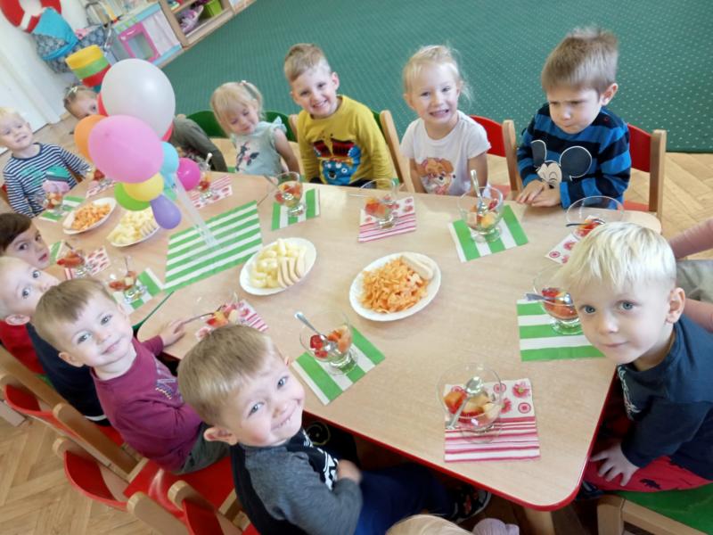 dzieci siedzą przy stole i częstują się smakołykami.