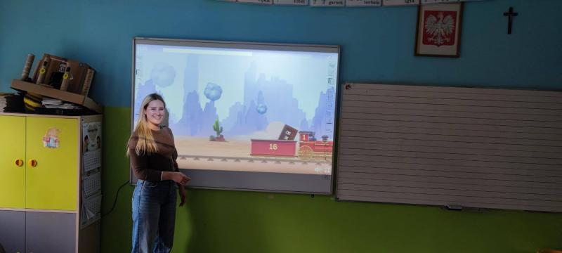 Nowa tablica interaktywna w sali edukacji wczesnoszkolnej pozyskana z kupon&oacute;w Szkoły Pełne Talent&oacute;w Lidla - edycja 4. Na zdjęciu pani Małgosia prowadzi lekcję z wykorzystaniem nowego sprzętu,