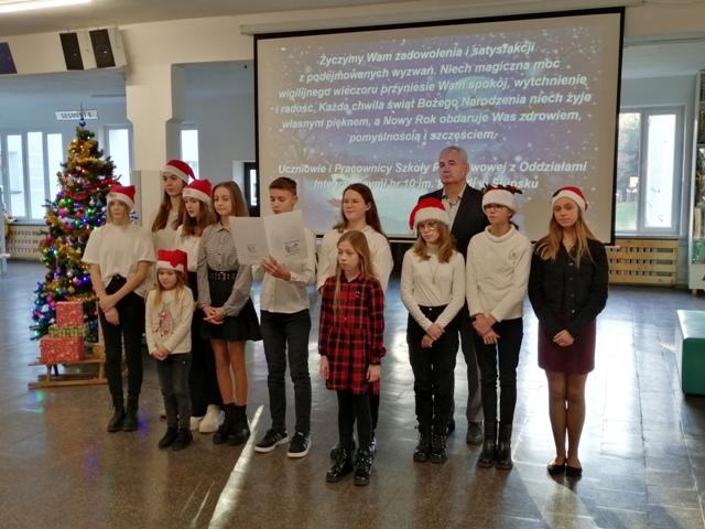 Dyrektor Szkoły, przedstawiciele Samorządu Uczniowskiego oraz zespół wokalny wraz z solistkami w holu głównym szkoły składają świąteczne życzenia.
