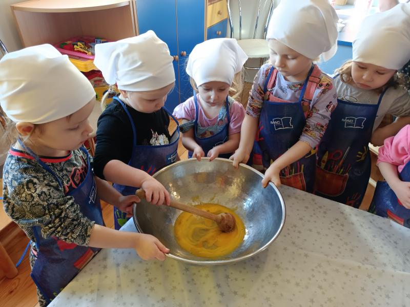 Dziewczynki w białych chustkach na głowie i fartuszkach mieszające produkty w dużej misce