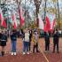 Szkolne boisko, opiekunka samorządu uczniowskiego z uczniami i flagami na szkolnym boisku inauguruje bieg o niepodległość