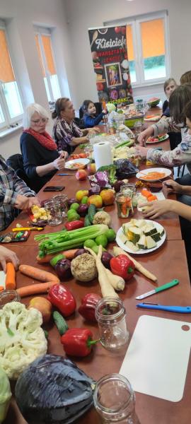 Na stole leżą noże i obieraczki, deski i słoiki. Leżą kolorowe warzywa i owoce. Wokół stołu siedzą mieszkańcy Reblina. Starsi jak i młodsi. Zaczynają kroić warzywa. Będziemy kisić.