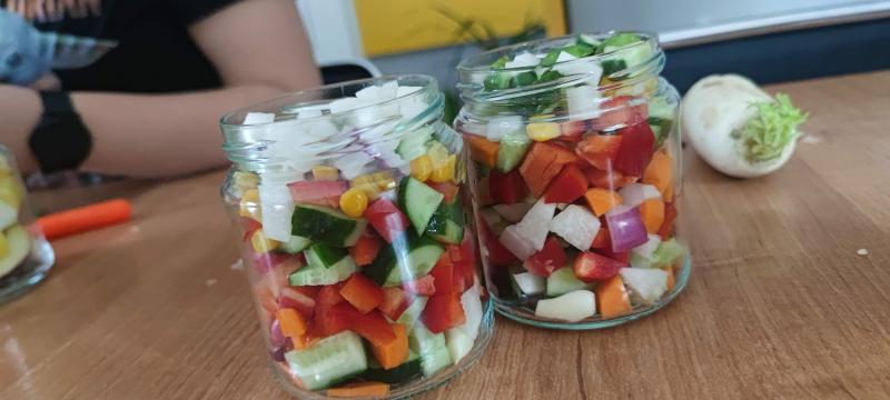 Dwa słoiki wypełnione kolorowymi pokrojonymi warzywami i owocami.