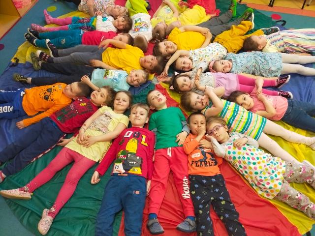 Zdjęcie przedstawia dzieci leżące na chuście animacyjnej podczas optymistycznej zabawy