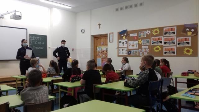 Policjanci i uczniowie w sali lekcyjnej w trakcie pogadanki na temat zasad bezpieczeństwa w miejscach pobytu dzieci.