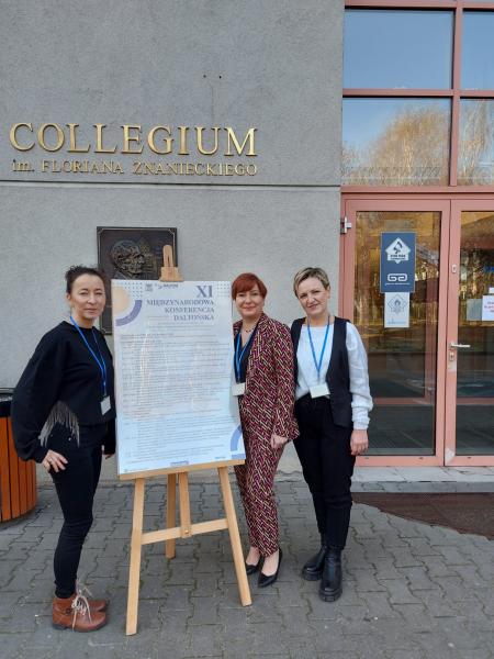 Na tle budynku Collegium im. Floriana Znanieckiego wraz z plakatem XI Międzynarodowej Konferencji Daltońskiej stoją trzy Panie.