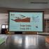 Na holu szkoły widzimy ekran ze slajdem informującym o święcie szkoły 2 maja 2021 roku. U góry slajdu widzimy złożoną flagę Polski z orłem na górze.