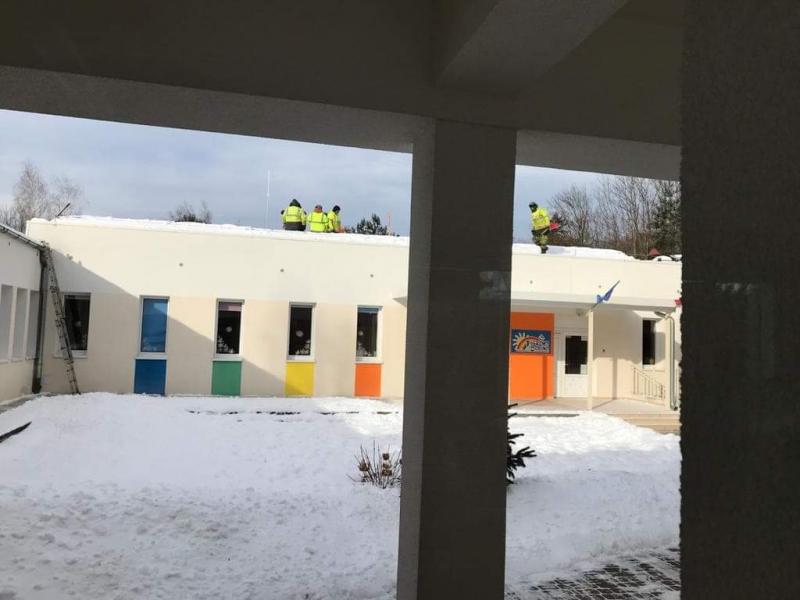 Na zdjęciu są mężczyźni w trakcie odśnieżania dachu budynku.