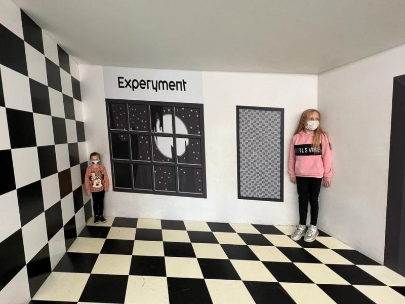 Dwie dziewczynki w pokoju złudzeń optycznych przeprowadzają eksperyment.