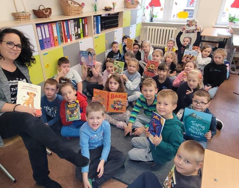 Dzieci siedzą na dywanie w szkolnej pracowni w dłoniach trzymają książki.