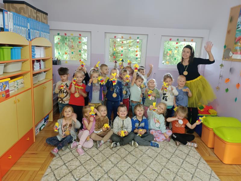Grupa dzieci wraz z nauczycielem. Dzieci mają na szyjach zawieszone medale a w ręku trzymają maskotkę zajączka