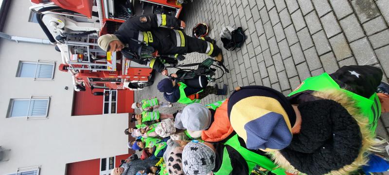 Strażak pokazuje dzieciom specjalny strój strażaka ubierany do akcji pożarniczej