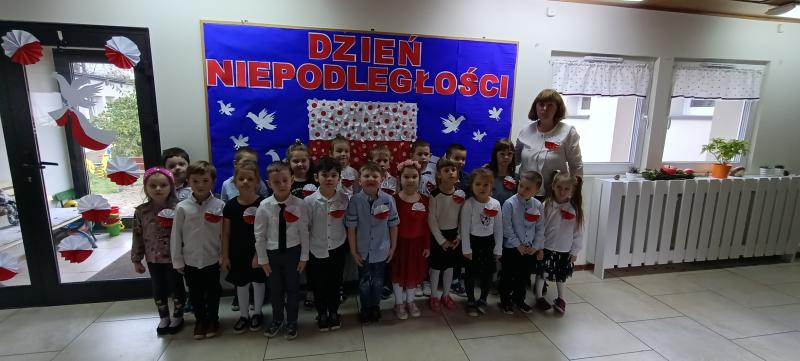 Wspólne odśpiewanie hymnu Mazurka Dąbrowskiego - dzieci ustawione w rzędach na holu, ubrane na galowo, w tle dekoracja z napisem 11 listopada i flagą polski