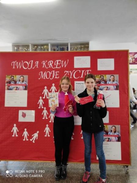 Wolontariuszki na tle tablicy promującej kampanię społeczną "Twoja krew, moje życie"