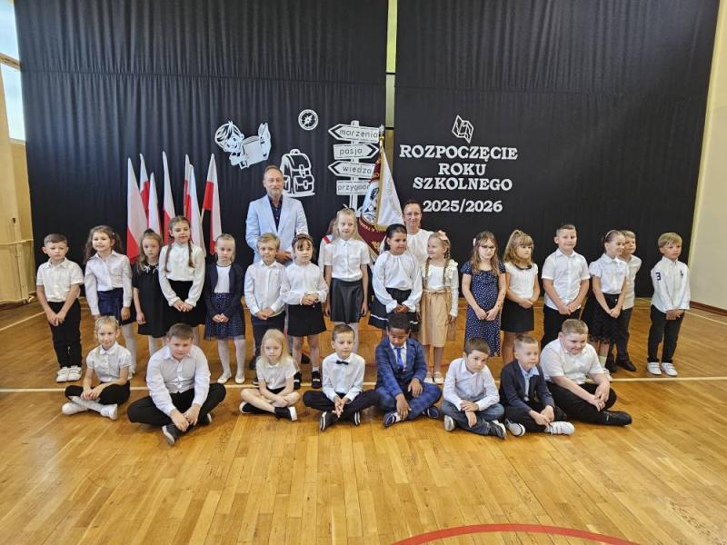 Rozpoczęcie roku szkolnego 2025/2026 z uroczystością pasowania na ucznia. Zdjęcie grupowe klasy 1a podczas uroczystości na sali gimnastycznej.