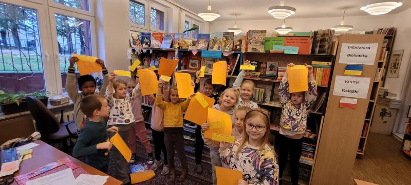 Pasowanie na czytelnika w bibliotece szkolnej. Uczniowie podnoszą do góry żółte kartki z regulaminem.