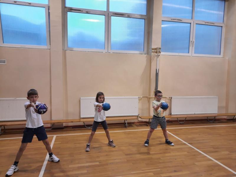 Uczniowie ćwiczą na sali gimnastycznej zabawy z piłką ręczną