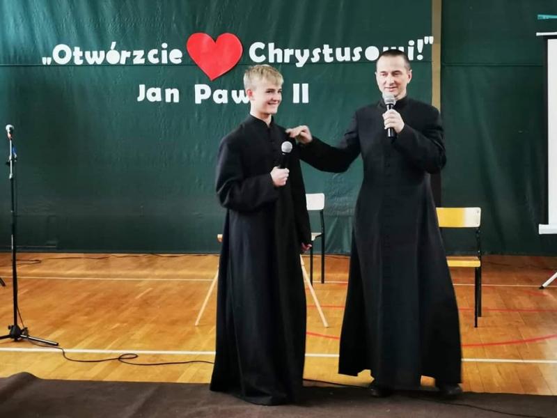 Dzień Papieski. Na scenie dużej sali gimnastycznej znajduje się ks. Andrzej wraz z aktorem - przebranym za księdza uczniem klasy siódmej.