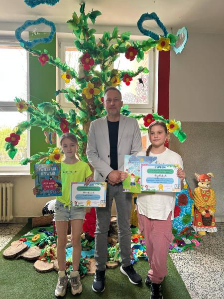 Na zdjęciu - dyrektor z nagrodzonymi uczennicami. W tle instalacja drzewa wiosennego szkolnego holu.